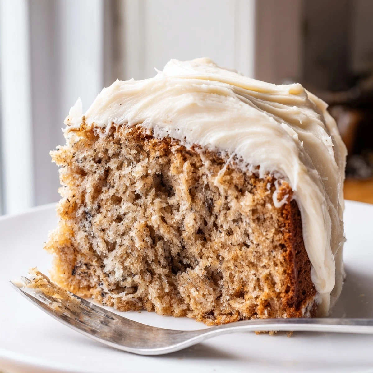 Warm brown butter banana cake slice with thick cream cheese frosting on rustic plate