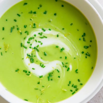 Vibrant green creamy asparagus soup with lemon in a white bowl, steam rising from the velvety puree.